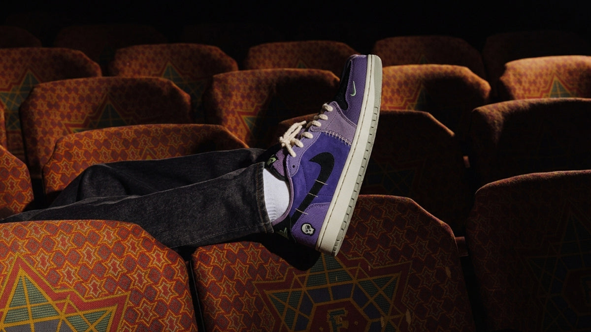Una pierna con unas Air Jordan 1 Low Voodoo Alternate apoyada en las butacas de un cine